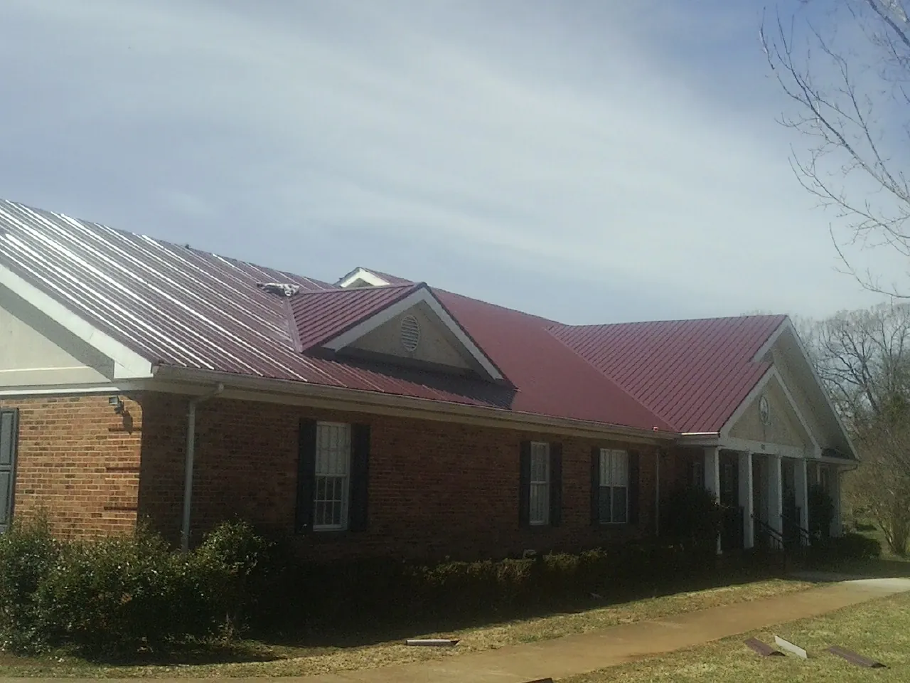 Red metal roof with gabled entries on a long brick building, from a Hail Damage Roof Repair job in Lemoore