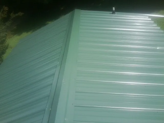 New green metal panels meeting at the ridge of a roof — Flat Roof Repair work by our crew in Lemoore