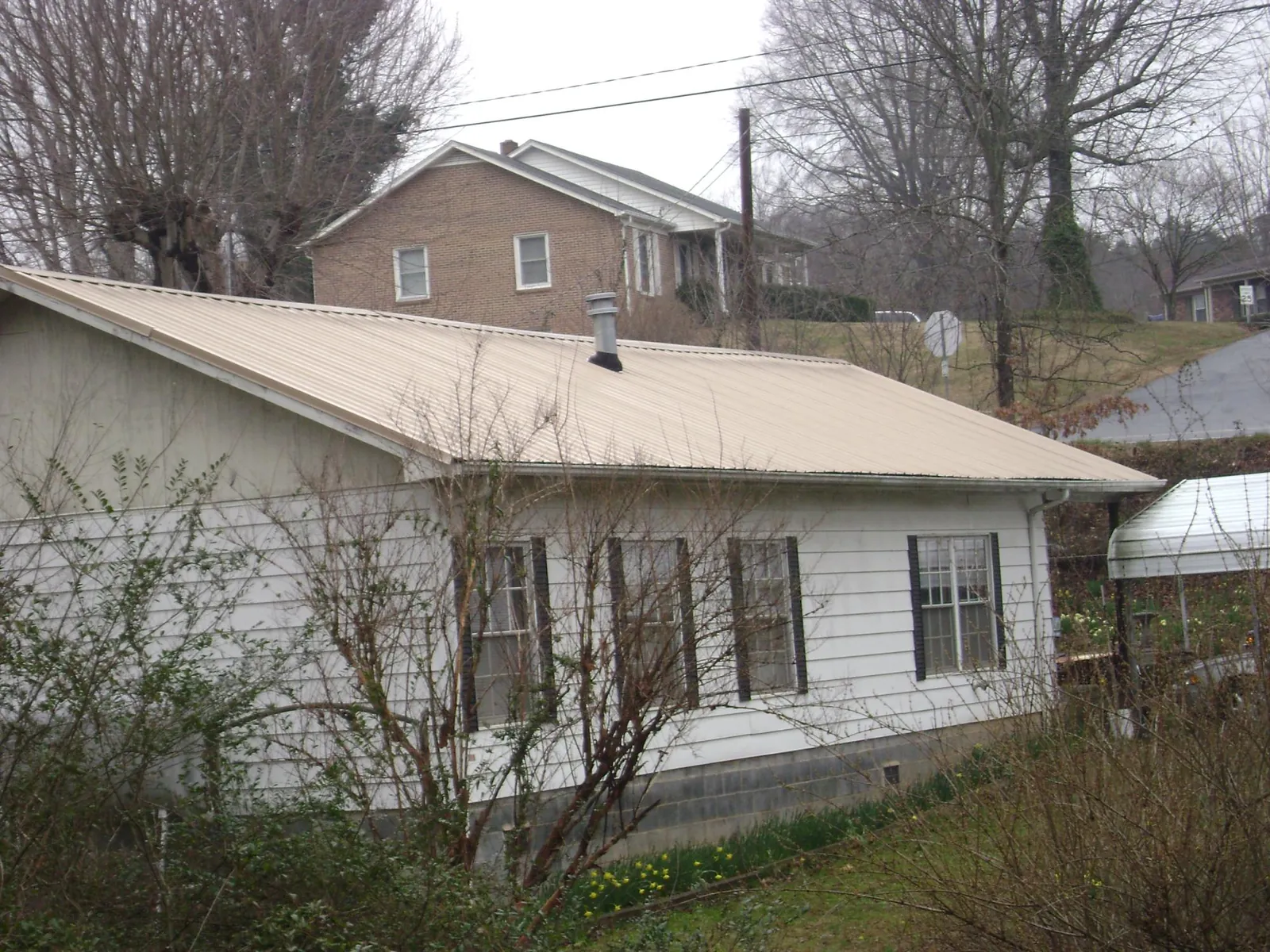 Tan metal roof on a white sided house set into a hillside — Commercial Roofing by Roofing Brothers in Lemoore